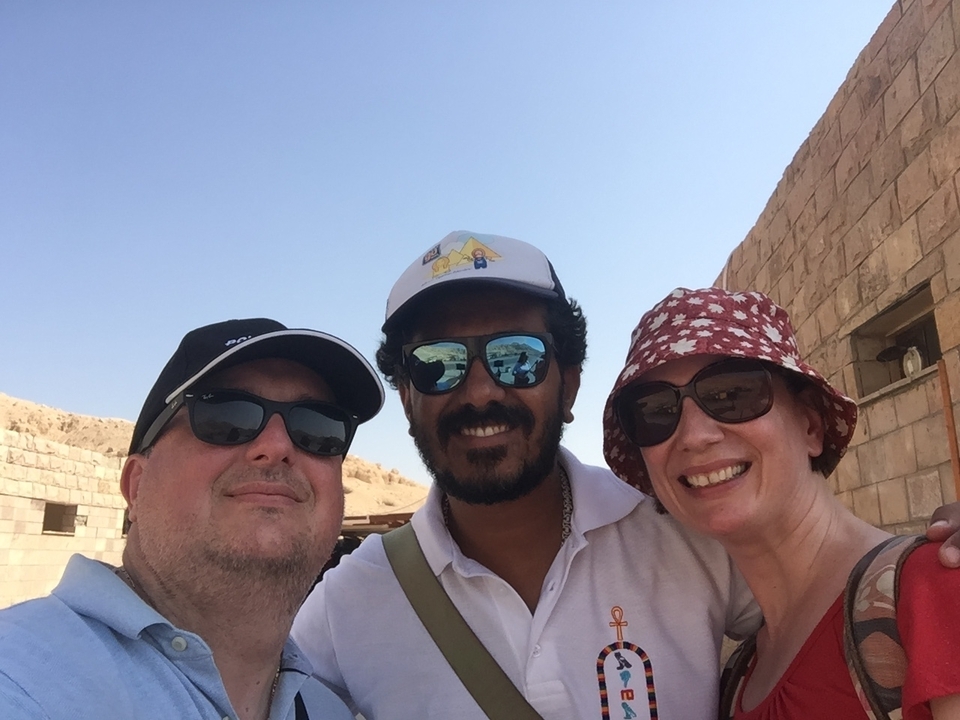 Trois personnes souriantes devant une structure de pierre ancienne.