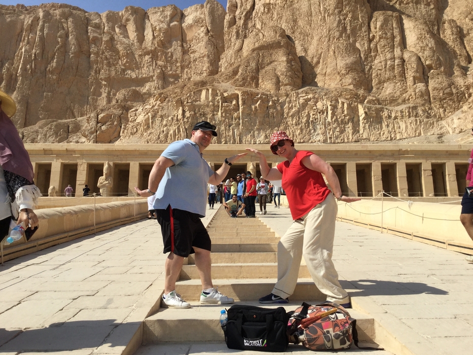 Deux touristes prenant la pose sur des escaliers avec un temple antique en arrière-plan.