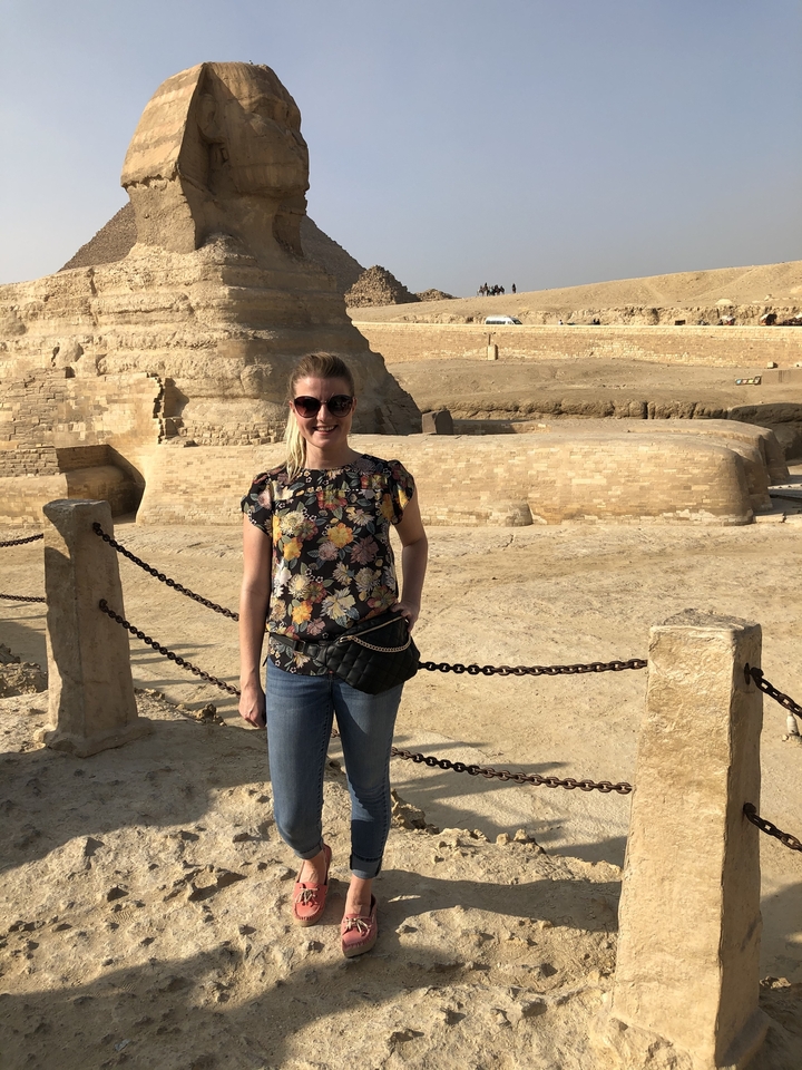 Femme posant devant une structure en pierre ancienne.