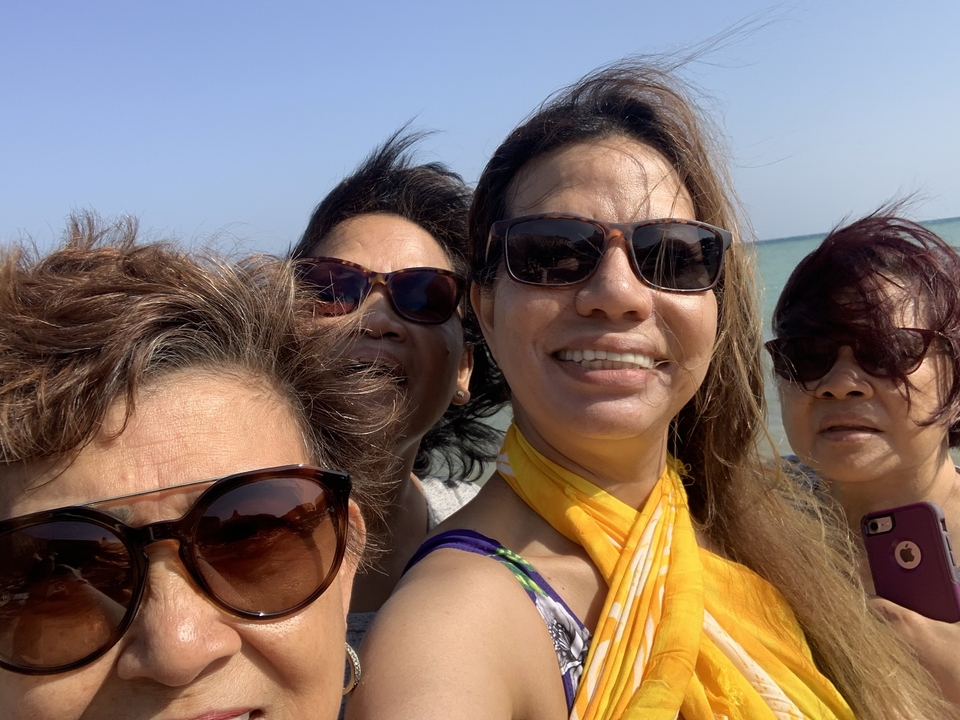 Quatre femmes souriantes à la plage avec le vent dans les cheveux.