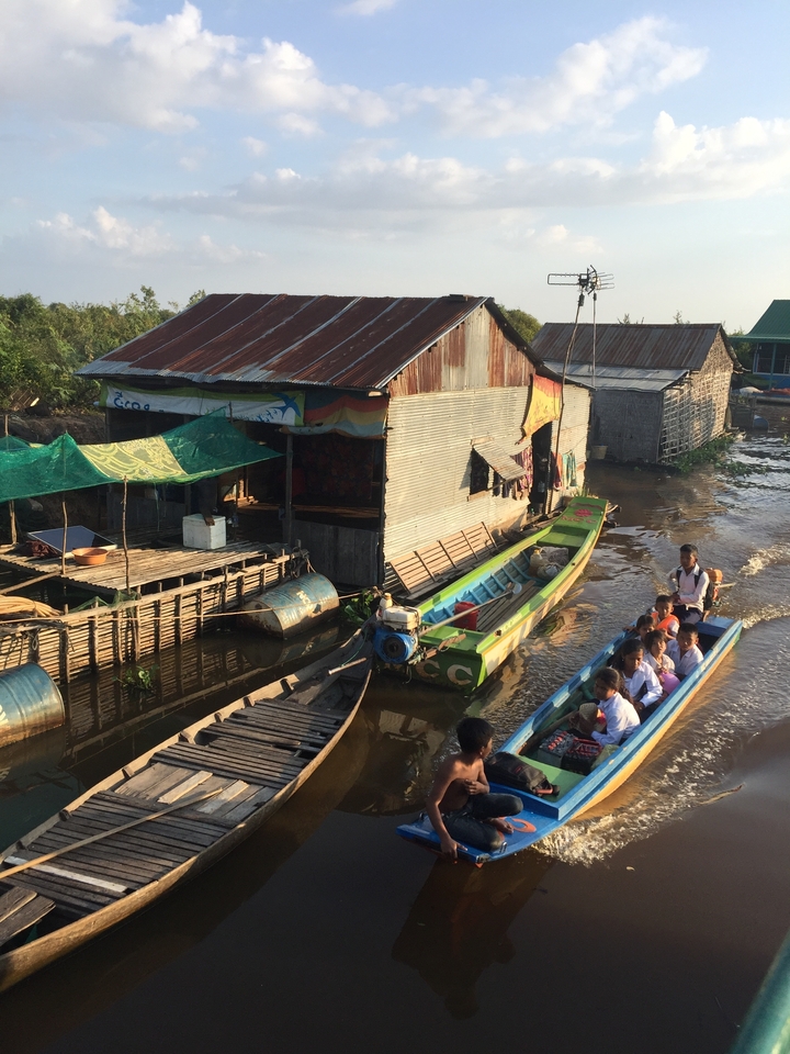 Des gens voyageant en bateau près de maisons sur pilotis dans un village flottant.