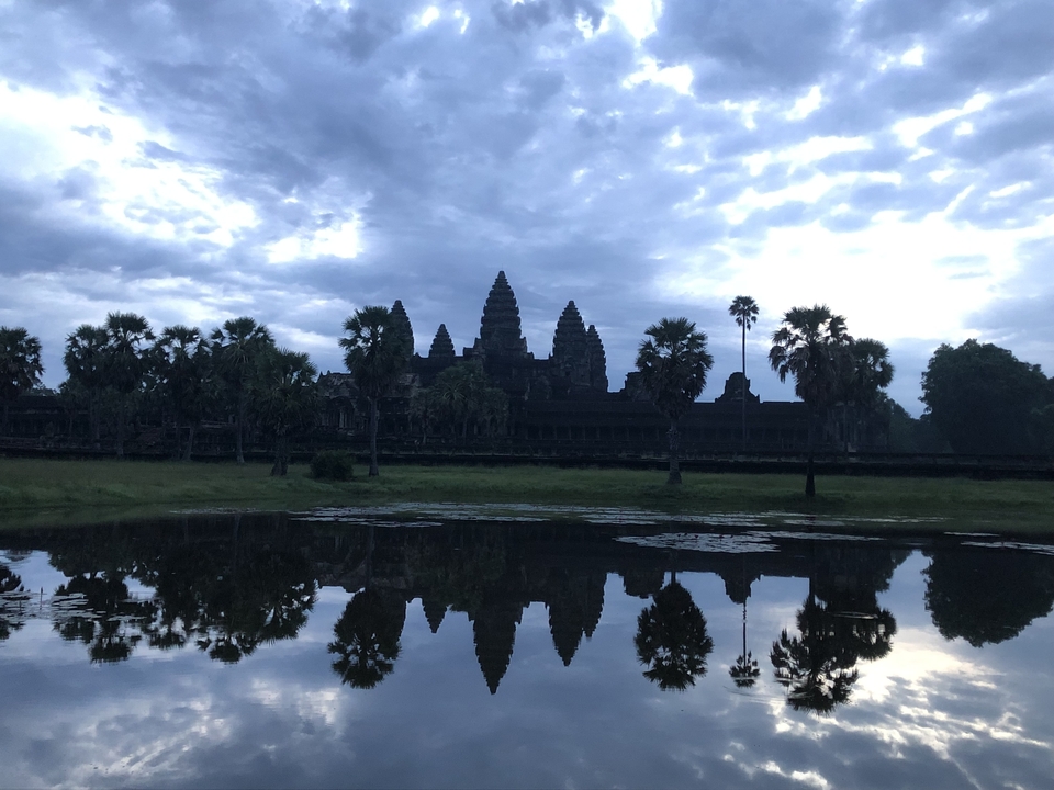 Angkor Wat en silhouette contre un ciel matinal avec un reflet dans l'eau.