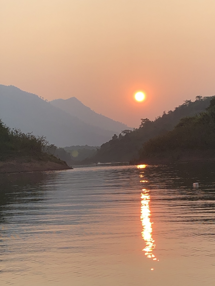 Vue panoramique d'une rivière au coucher du soleil avec des collines en silhouette.