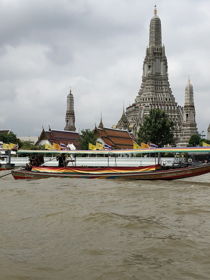 Bateau à longue queue thaïlandais avec un temple en arrière-plan le long d'une rivière.