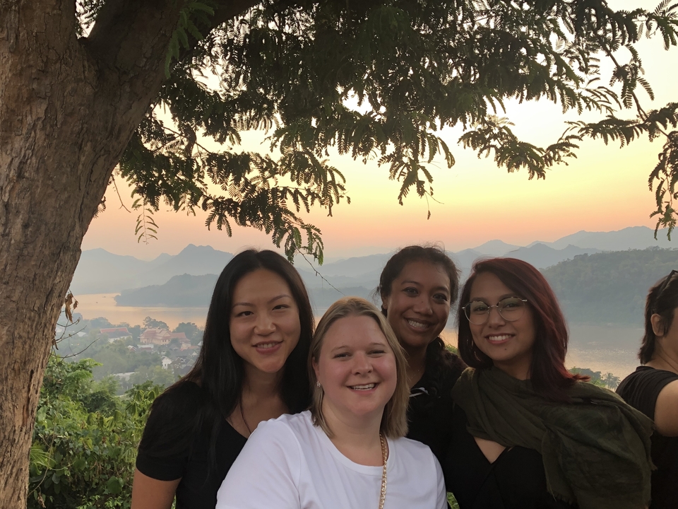 Quatre femmes posant sous un arbre avec un paysage pittoresque.