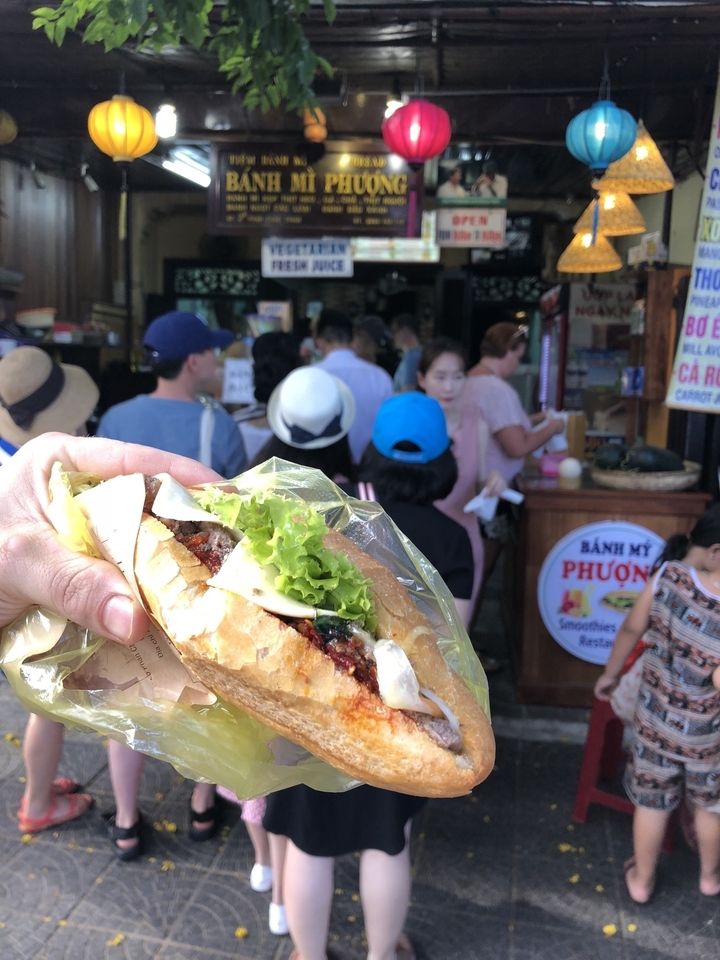 Gros plan d'une personne tenant un sandwich banh mi avec une foule en arrière-plan.