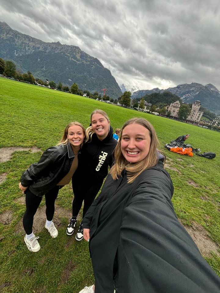 Trois femmes posant à l'extérieur avec une végétation montagneuse verdoyante.