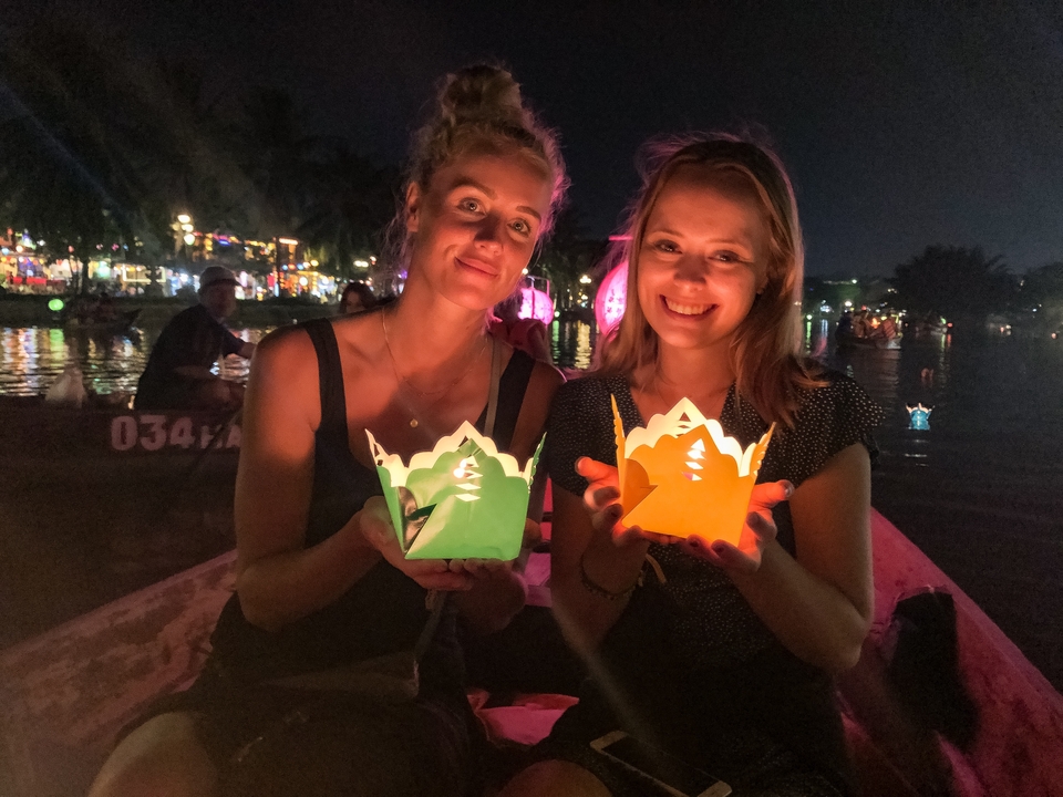 Deux femmes tenant joyeusement des lanternes en papier dans un bateau la nuit.