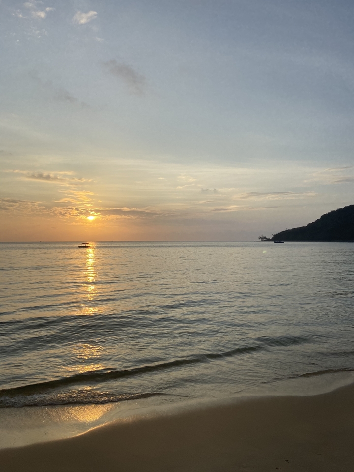 Vue du coucher de soleil sur une mer calme avec un bateau solitaire.