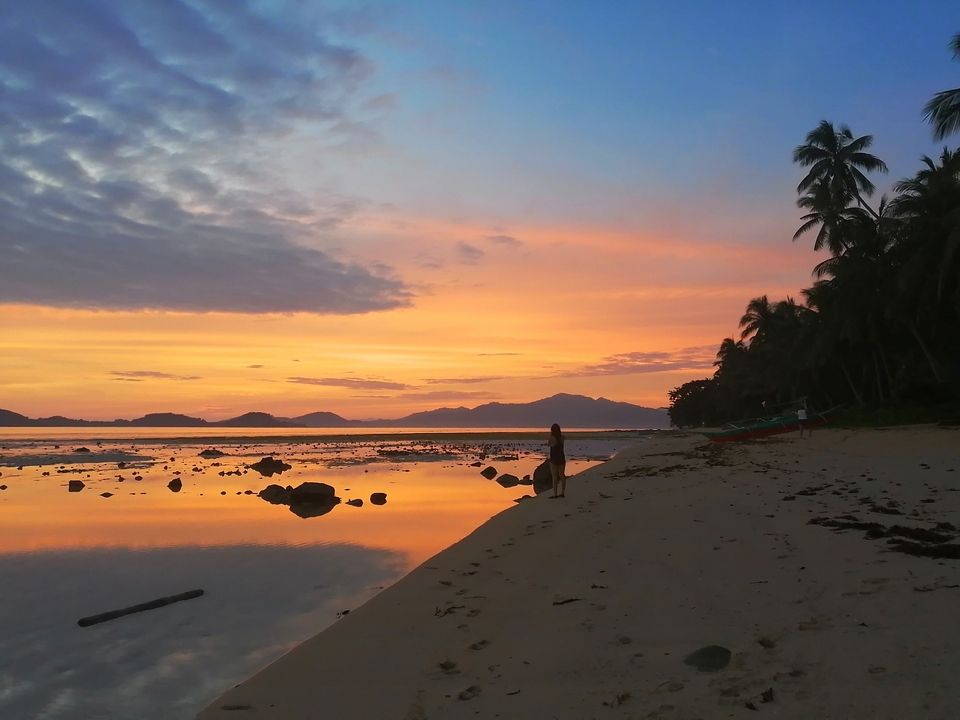 Magnifique coucher de soleil sur la plage avec la silhouette d'une personne et des palmiers.