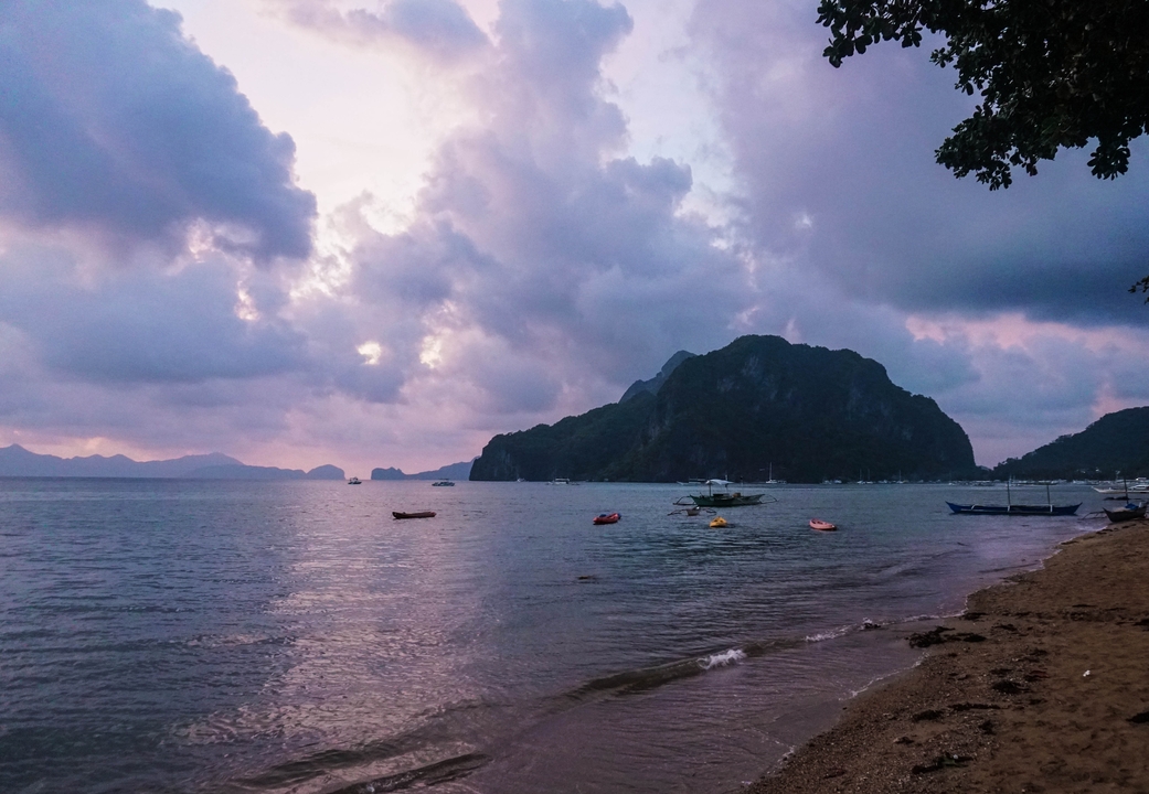 Coucher de soleil nuageux sur une plage avec des bateaux aux alentours.