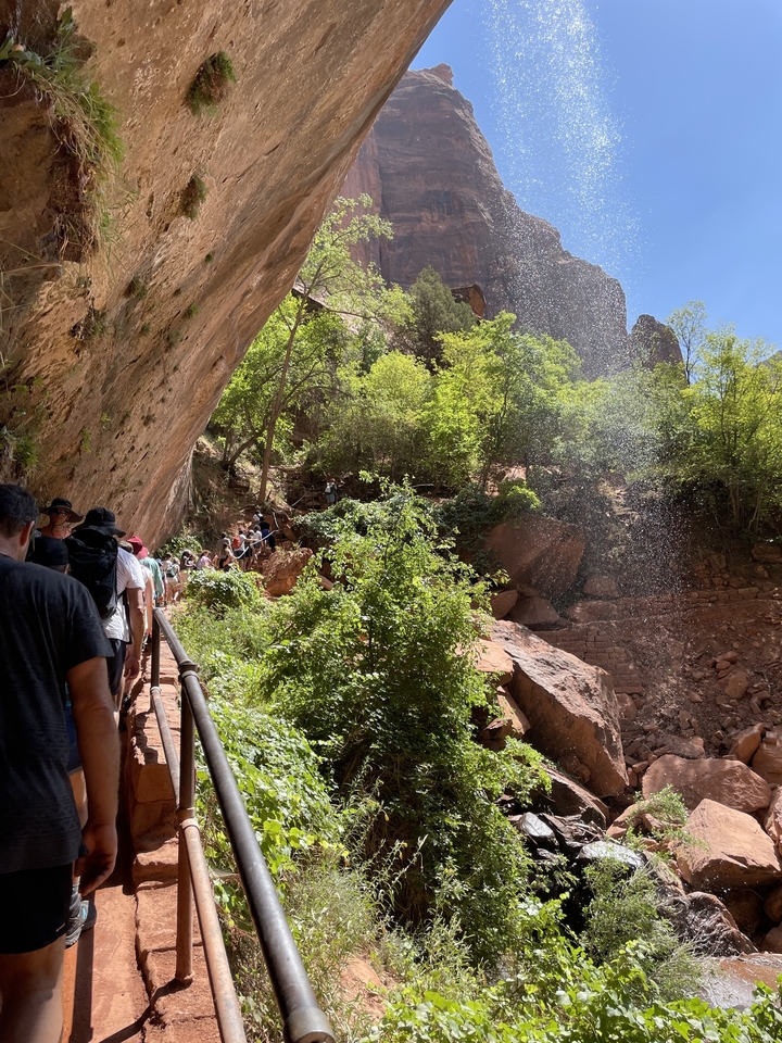 Randonnée en groupe sur un sentier sous un surplomb rocheux avec des embruns de cascade.