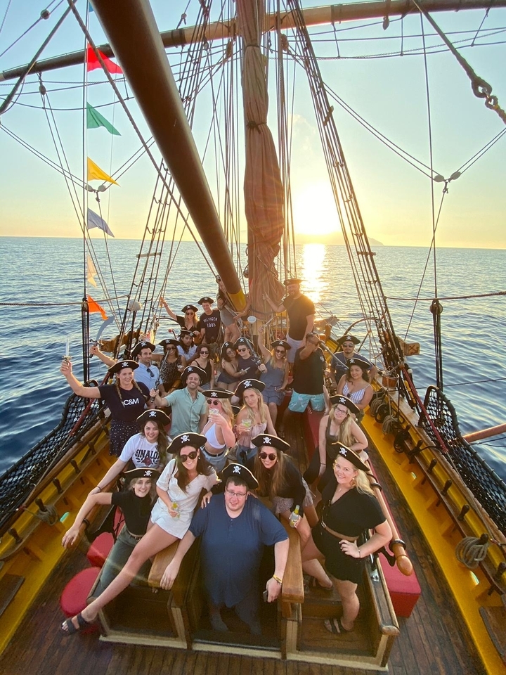 Group posing on a pirate-themed ship at sunset.