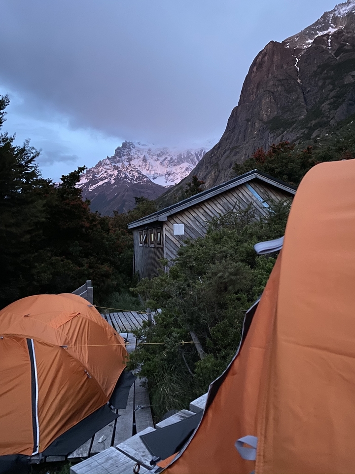 Terrain de camping avec des tentes et un petit bâtiment en bois dans une zone montagneuse.
