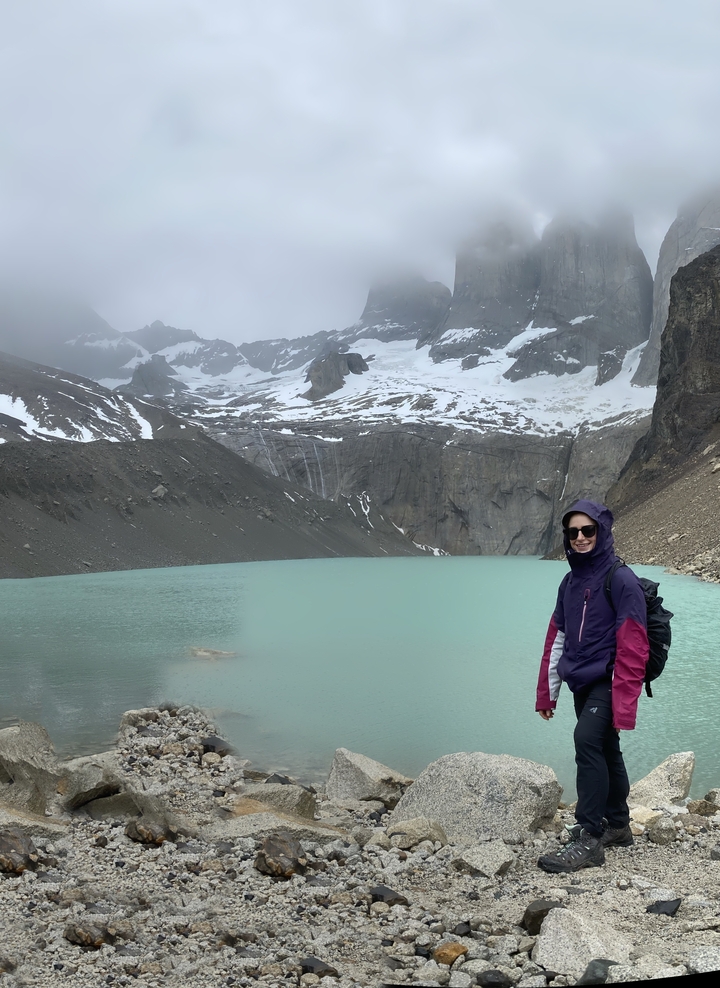 Randonneu-r/-se debout près d'un lac turquoise avec des montagnes enneigées au-delà.