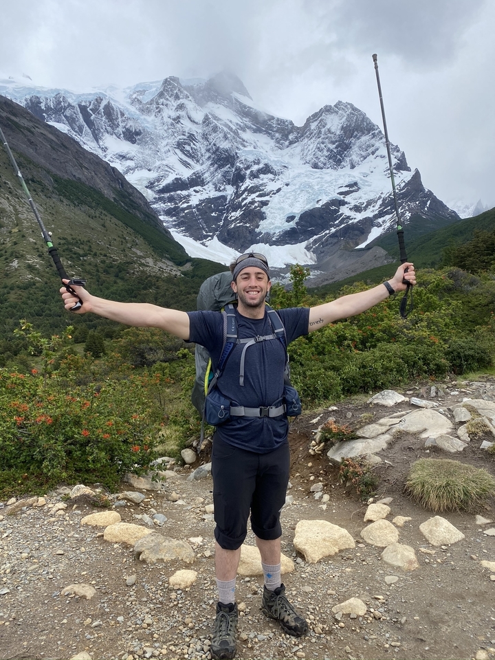 Randonneur avec les bras levés devant un glacier.