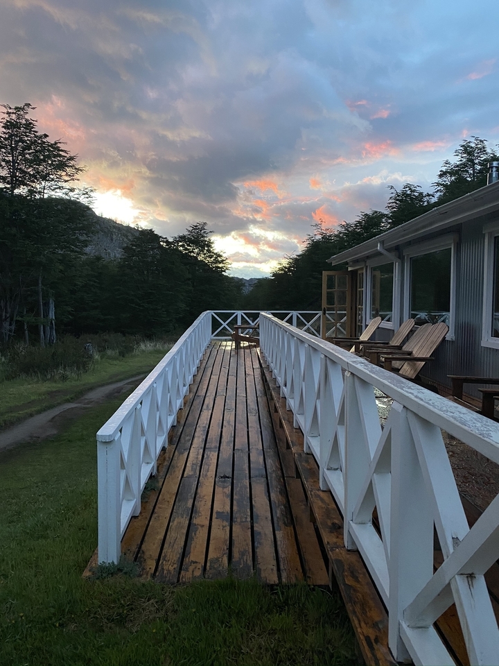 Passerelle en bois menant à une maison avec un coucher de soleil pittoresque en arrière-plan.