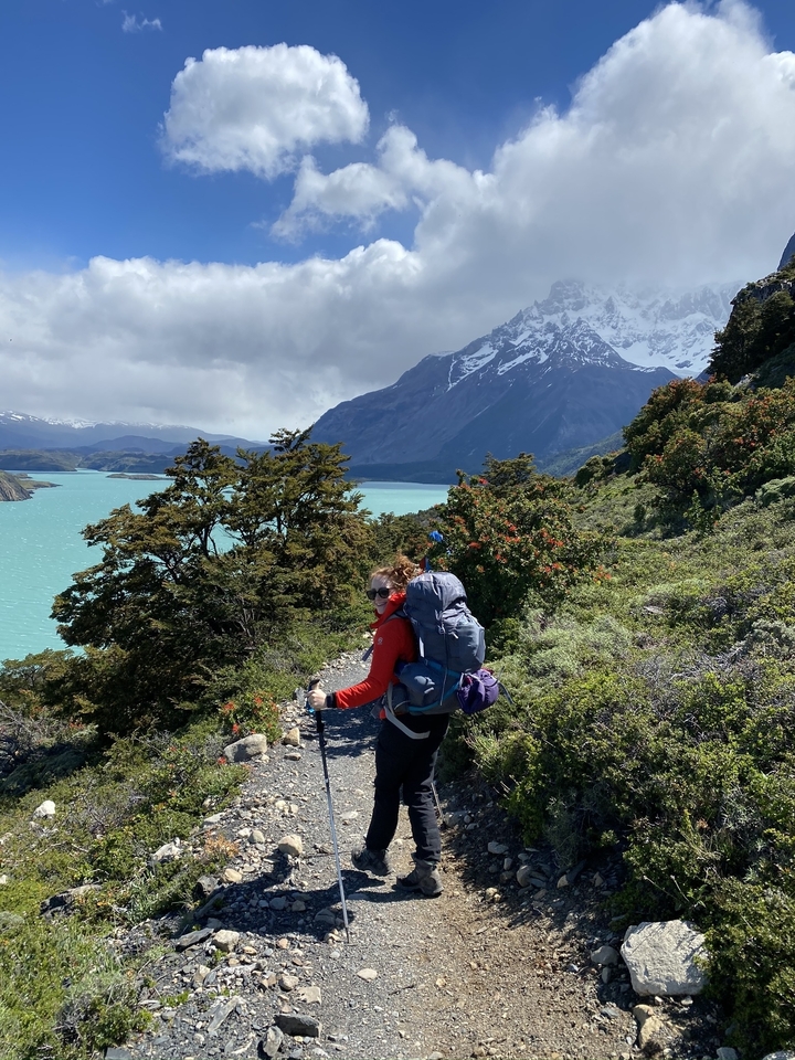 Randonneurs avec sac à dos marchant sur un sentier au bord d'un lac avec des montagnes.