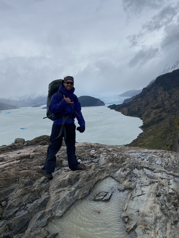 Randonneur sur une falaise au-dessus d'un grand lac avec des icebergs en arrière-plan.