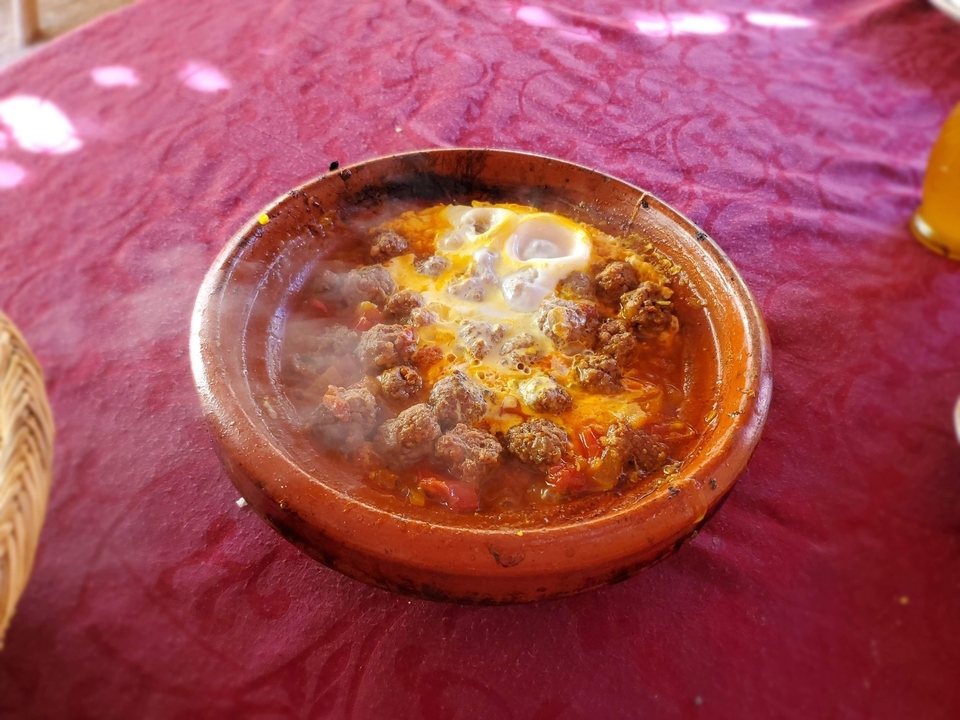 Plat marocain avec boulettes de viande et œufs dans un pot en terre cuite.