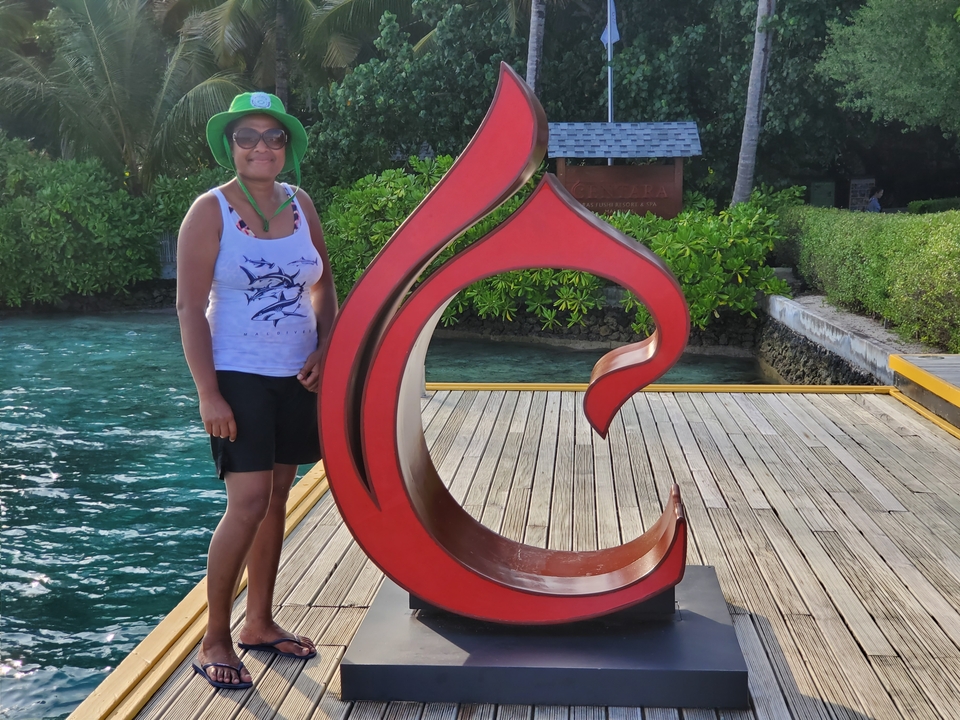 Femme posant à côté d'une sculpture rouge au bord de l'eau.