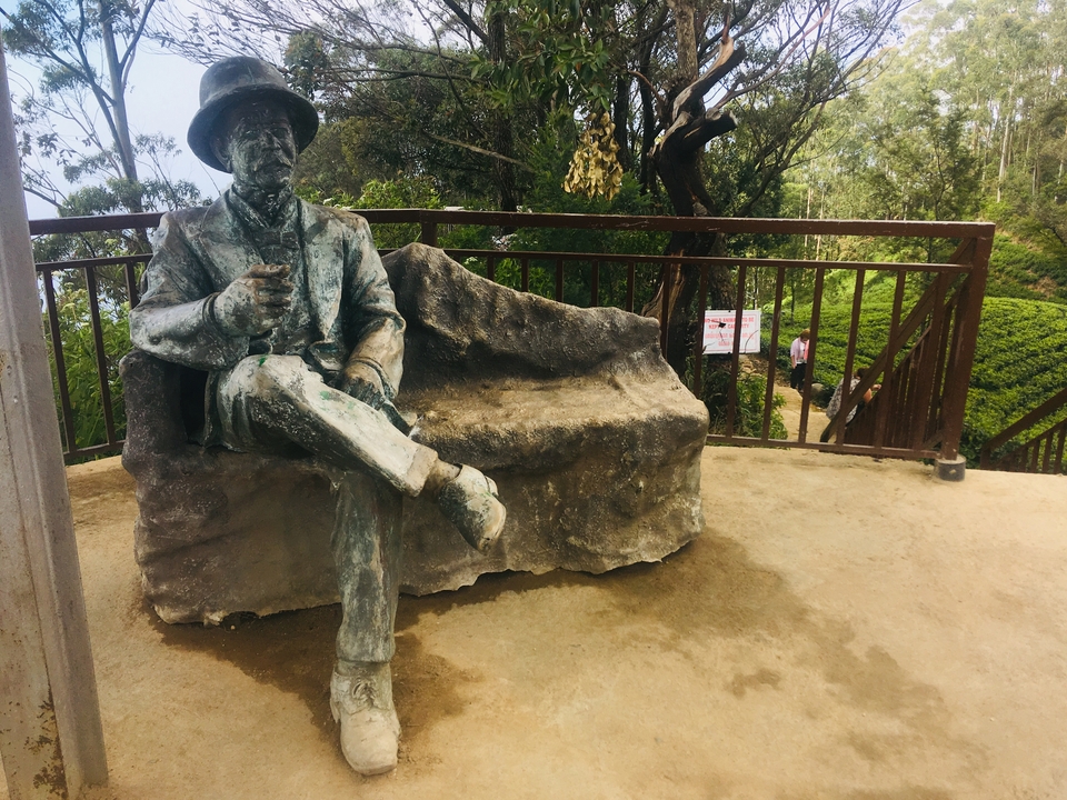 Statue d'une personne assise sur un banc dans un parc.