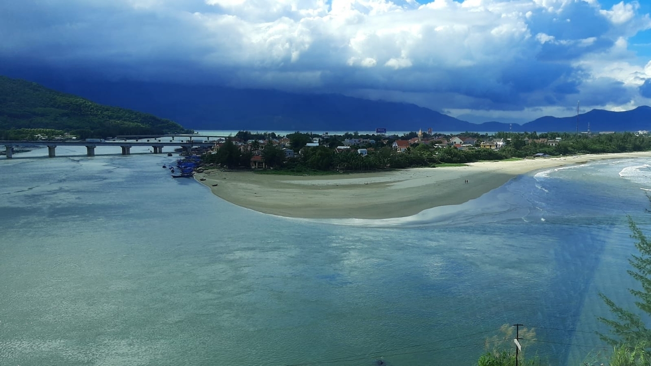 Vue panoramique d'une rivière qui rejoint une plage sous un ciel nuageux.