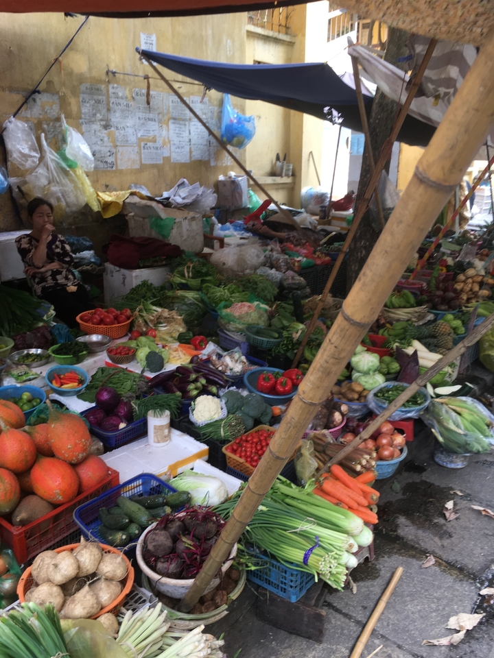 Un étal de marché animé avec des légumes variés et une femme assise à proximité.