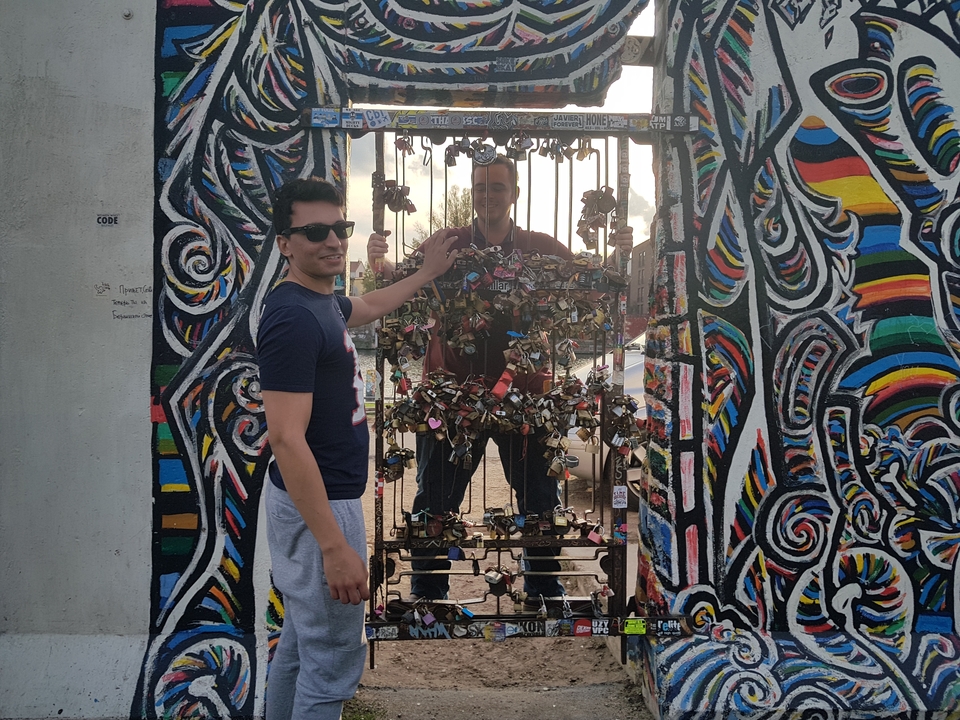 Two people posing at a colorful mural with locks attached.