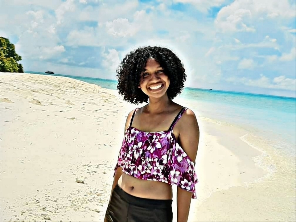 Personne heureuse qui pose sur une plage de sable blanc avec l'océan en arrière-plan.