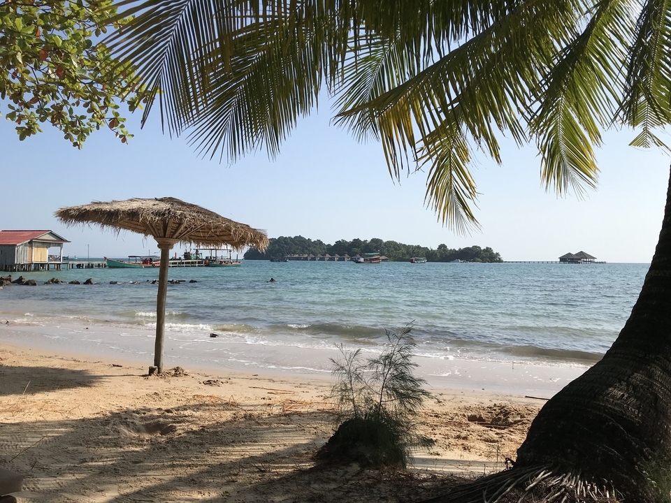 Scène de plage ensoleillée avec un parasol en chaume et des îles au loin.
