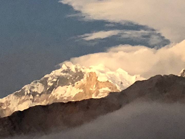 Pico de montaña iluminado por el sol con nubes al fondo.
