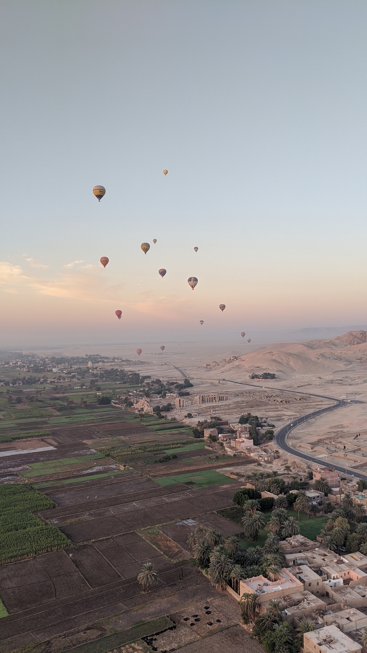 Des ballons flottant au-dessus d'un paysage avec des collines lointaines et un lever de soleil.
