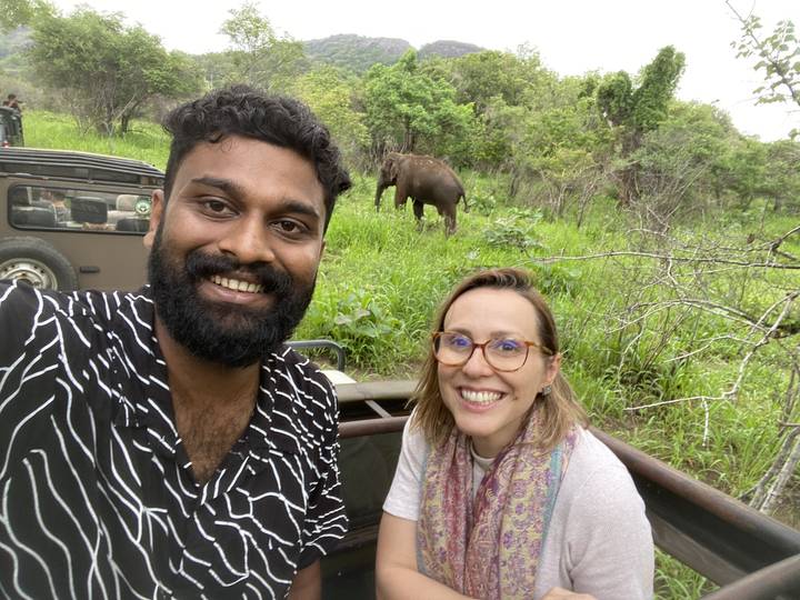 Deux personnes souriantes avec un rhinocéros en arrière-plan.
