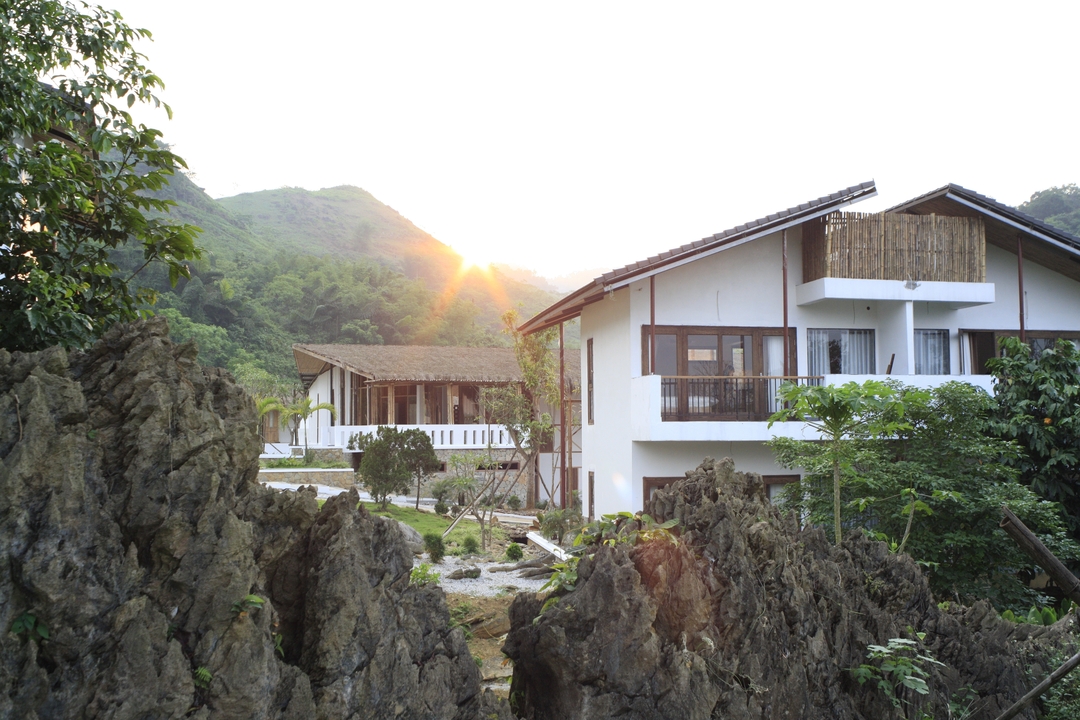 Soleil couchant derrière une maison avec des montagnes en arrière-plan.