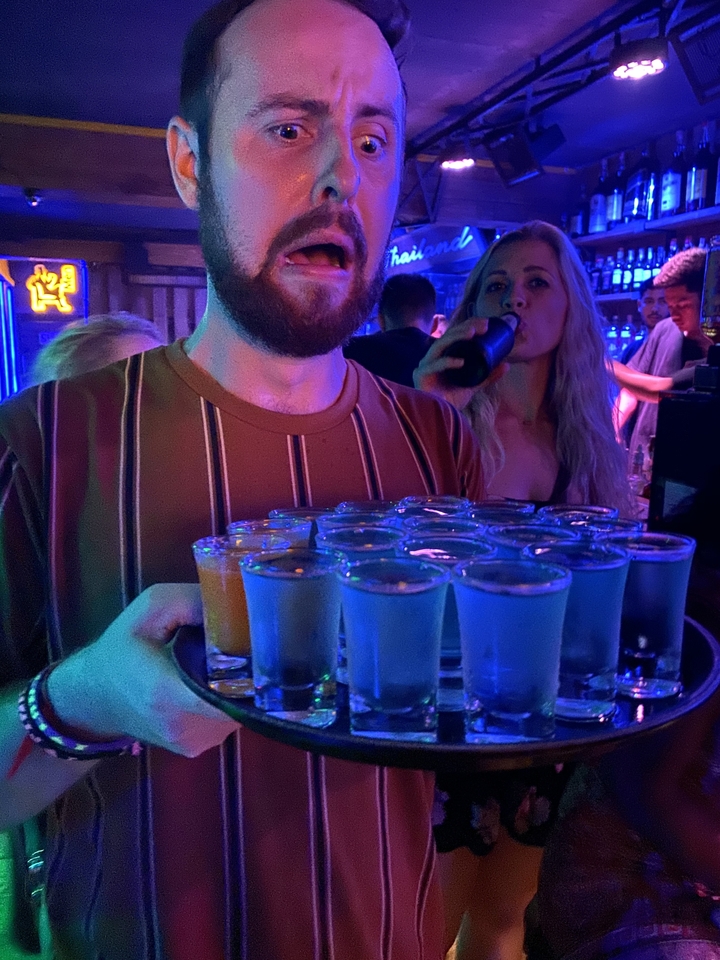 Personne tenant un plateau avec plusieurs verres à shot dans un bar.