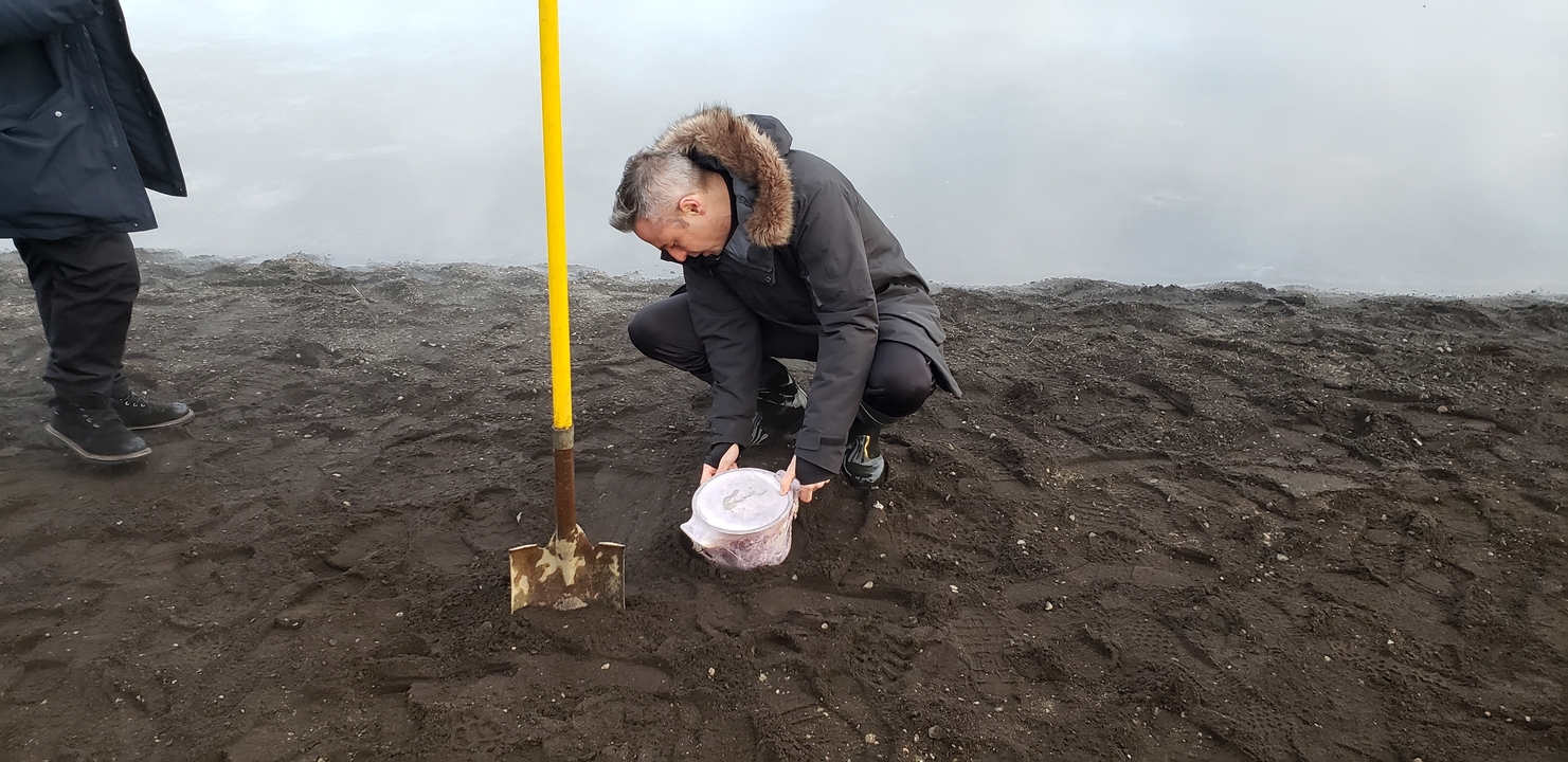 Person squatting on the ground with container and shovel.