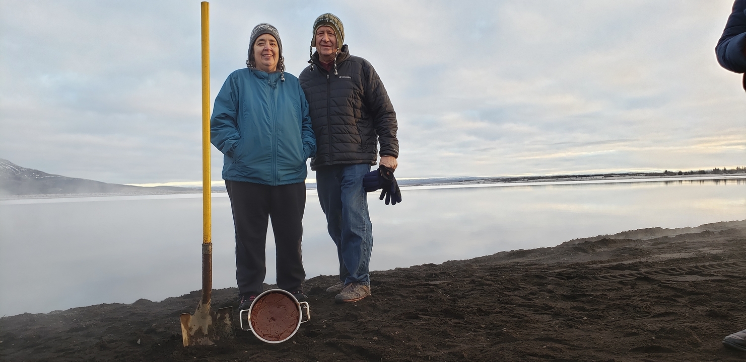 Two people standing near a misty body of water with a shovel in the ground.