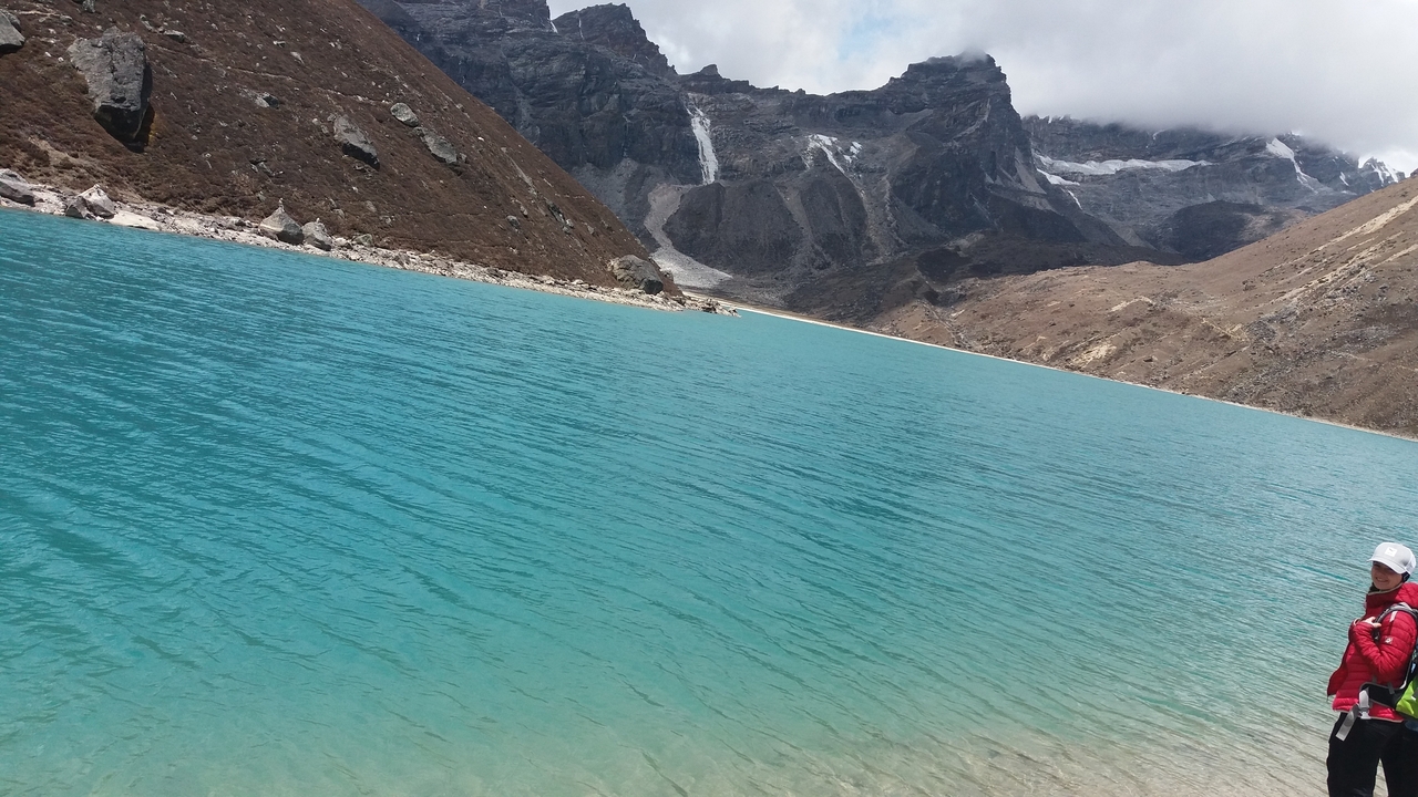 Personne debout près d'un lac bleu vibrant dans une région montagneuse.