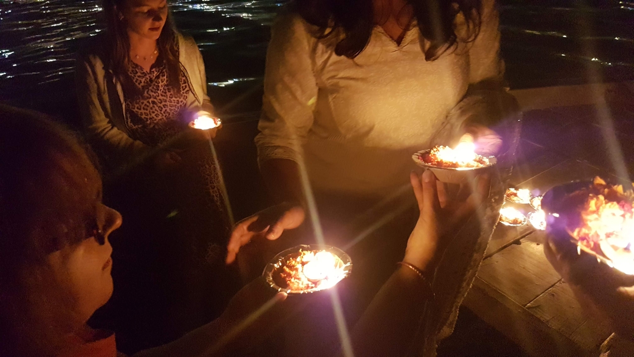 Des personnes tenant des offrandes aux chandelles au-dessus de l'eau la nuit.