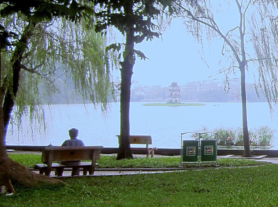 Une personne assise sur un banc au bord du lac avec une île.