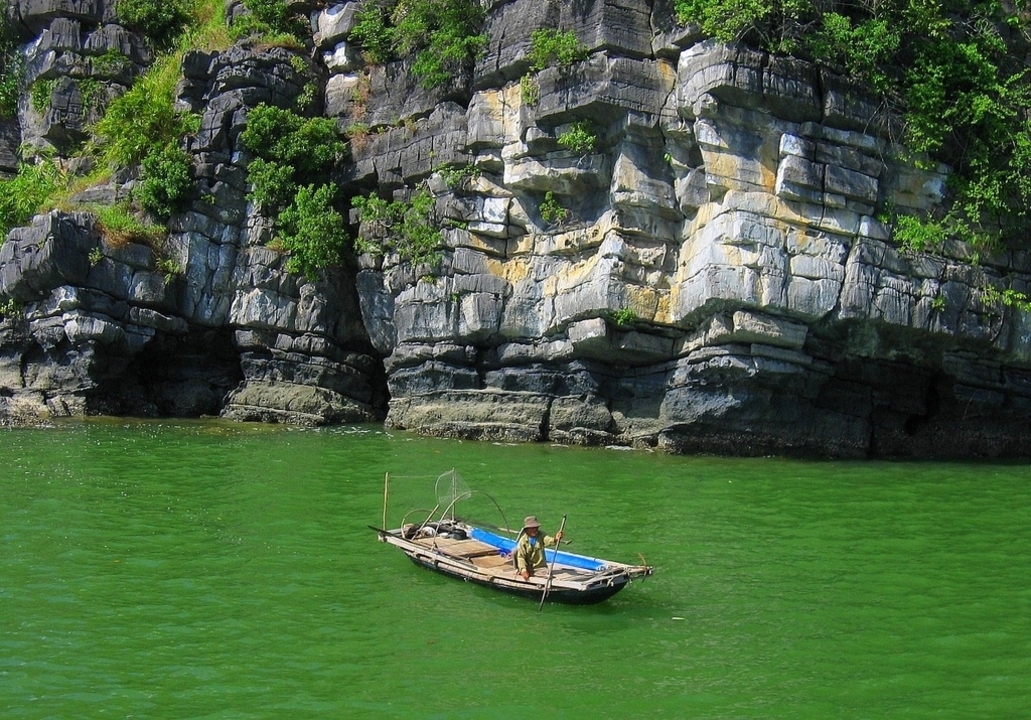 Une personne dans un petit bateau sur de l'eau verte entourée de falaises.