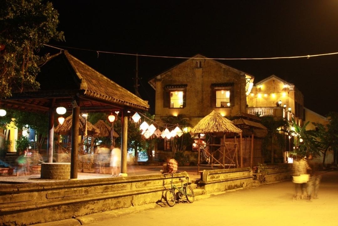 Scène de nuit à Hoi An avec des lanternes et des silhouettes floues.