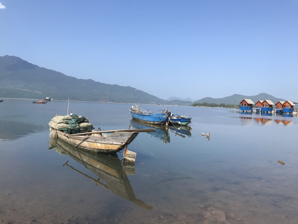 Lac serein avec des bateaux et des cabanes en bois, entouré de montagnes.