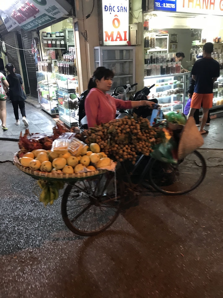 Personne faisant du vélo chargé de fruits dans une rue.