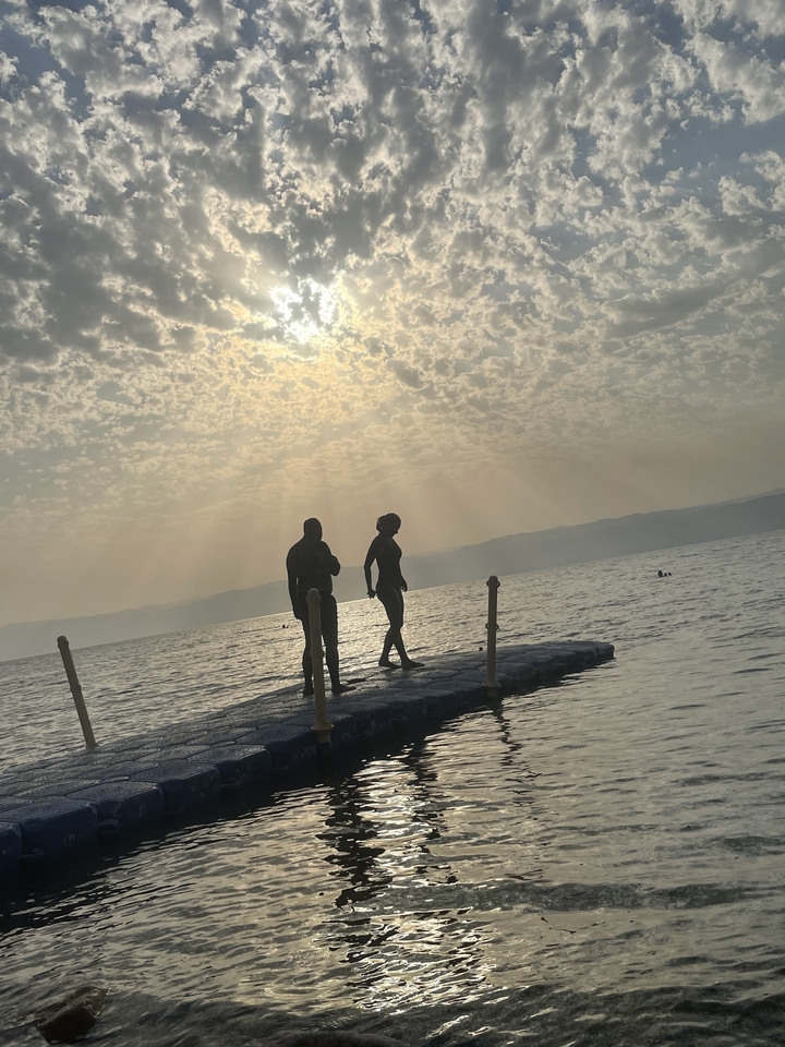 Silhouettes de deux personnes marchant sur une plateforme au-dessus de l'eau.