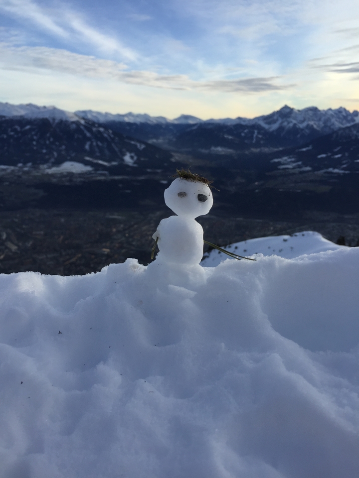 Gros plan d'un petit bonhomme de neige avec des brindilles en guise de bras sur une montagne enneigée.