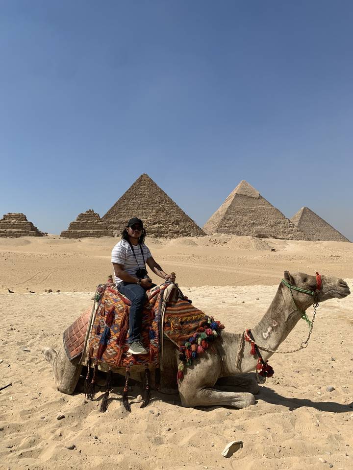 Personne à dos de chameau avec des pyramides en arrière-plan.