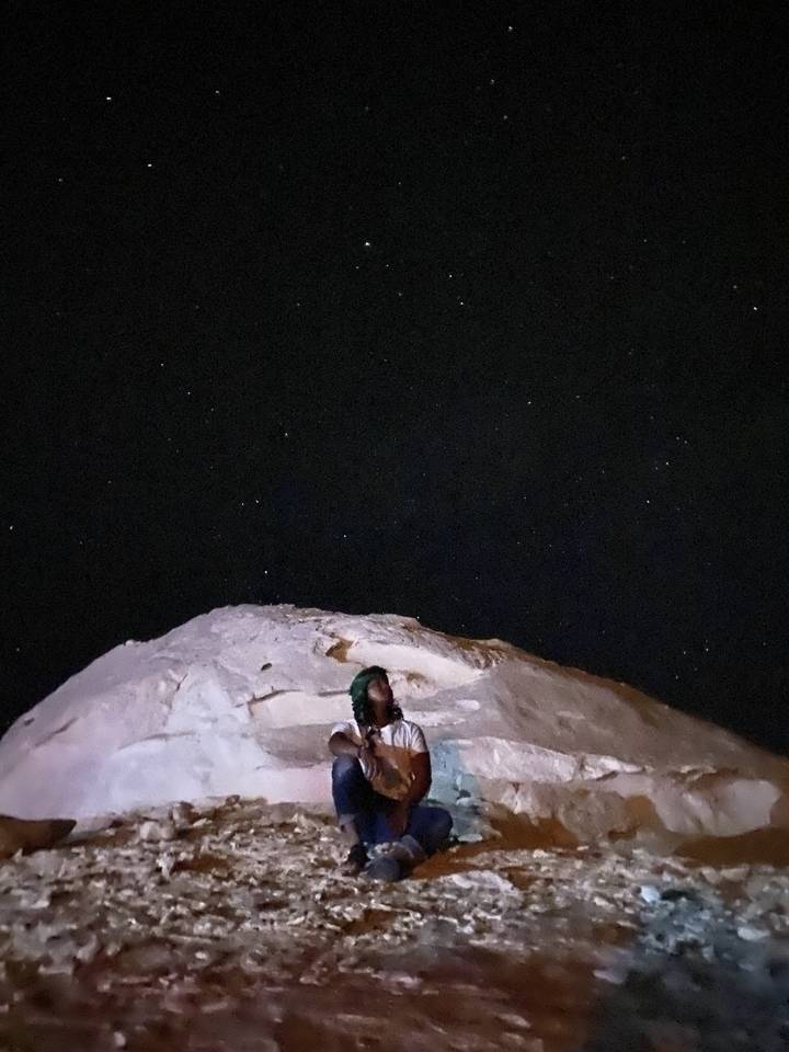 Personne assise près des rochers sous un ciel étoilé.