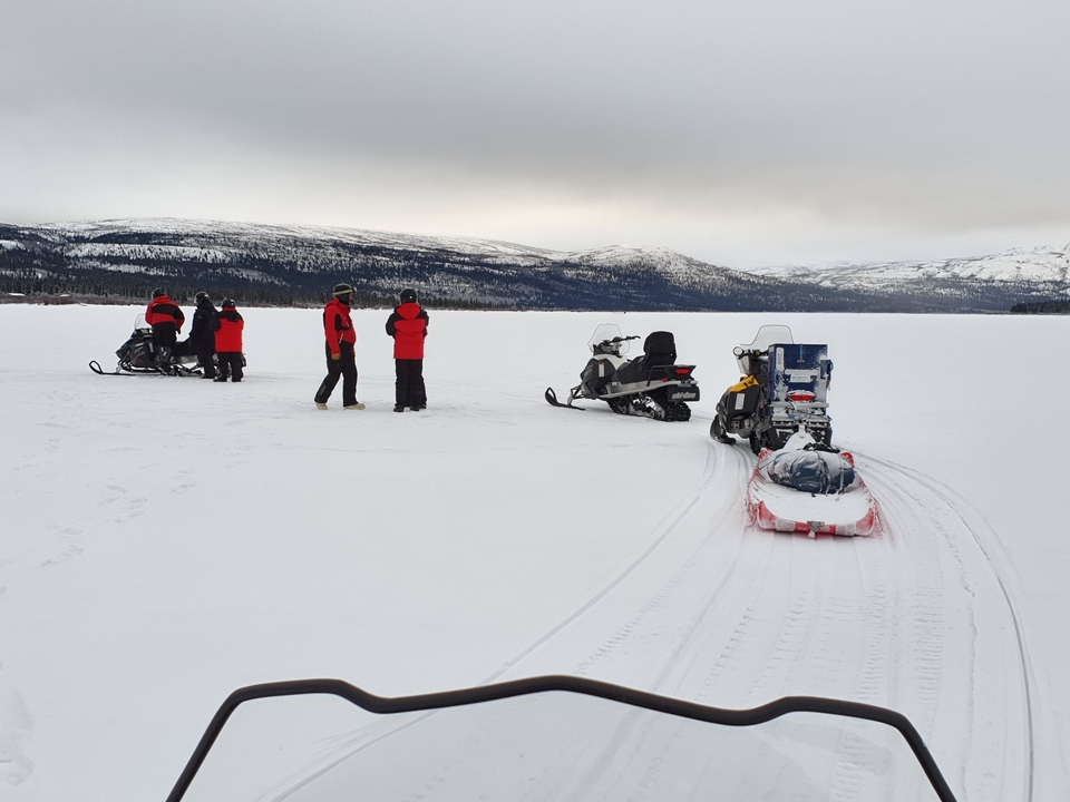 Personnes sur des motoneiges sur un lac gelé avec des montagnes enneigées